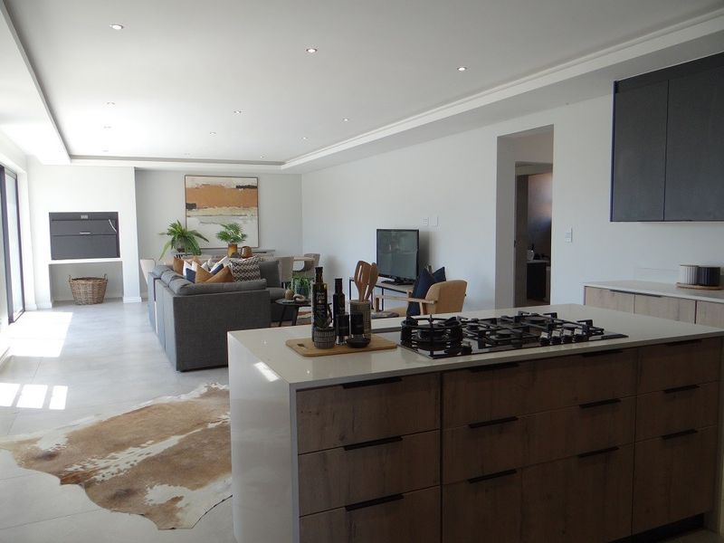 Modern open-plan living area featuring a sleek kitchen island with gas cooktop, tiled floors, recessed lighting, and a built-in fireplace.