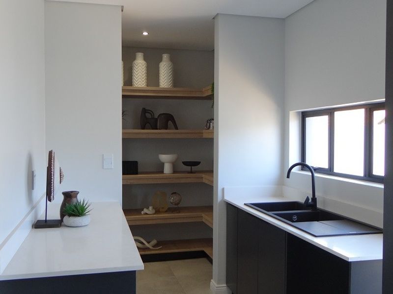 Modern scullery featuring sleek dark cabinetry, white stone countertops, an undermount sink with black tapware, and integrated open timber shelving.