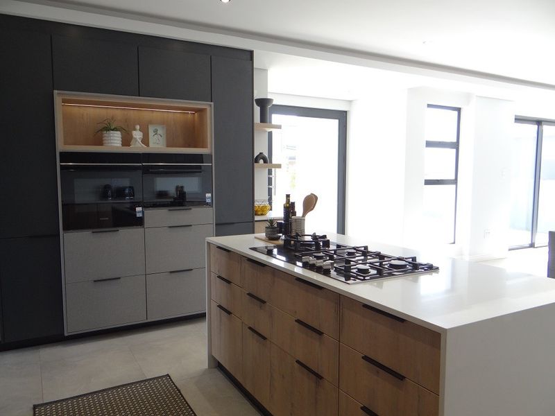 Modern kitchen featuring a central island with a gas cooktop, sleek two-tone cabinetry, built-in ovens, and high-quality stone countertops.