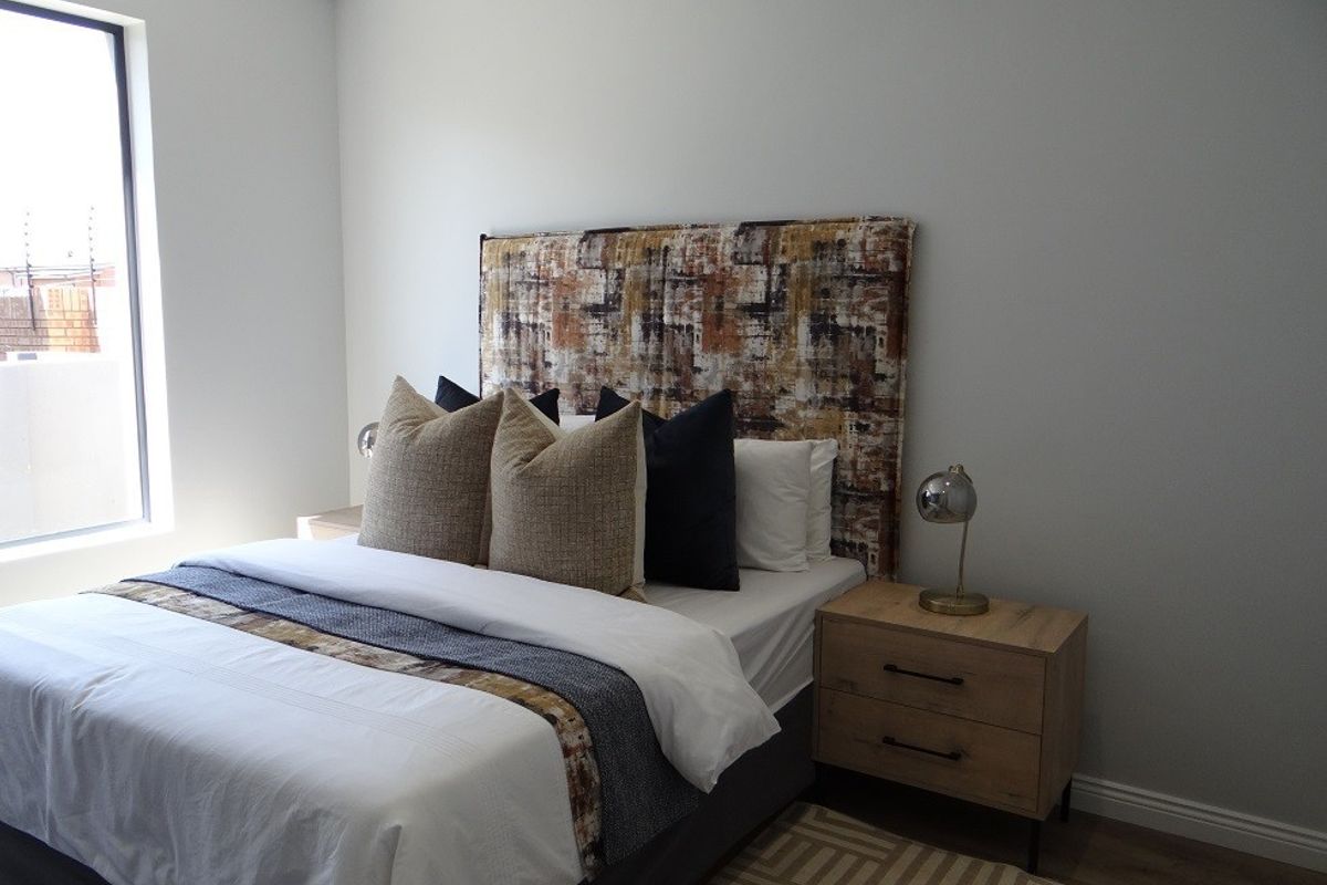 A well-lit bedroom featuring neutral walls, laminate flooring, and a large vertical window providing natural light.