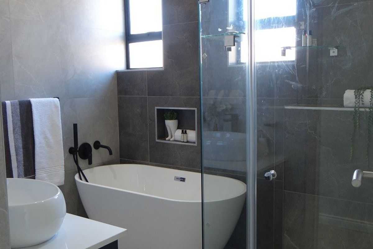 Modern bathroom featuring a sleek freestanding bathtub, a glass-enclosed shower, dark grey wall tiling, and a contemporary vanity basin with wall-mounted fixtures.