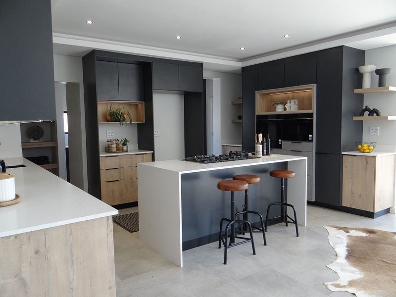 Modern kitchen featuring a central island with a gas cooktop, sleek dark cabinetry, light wood accents, and high-quality stone countertops.