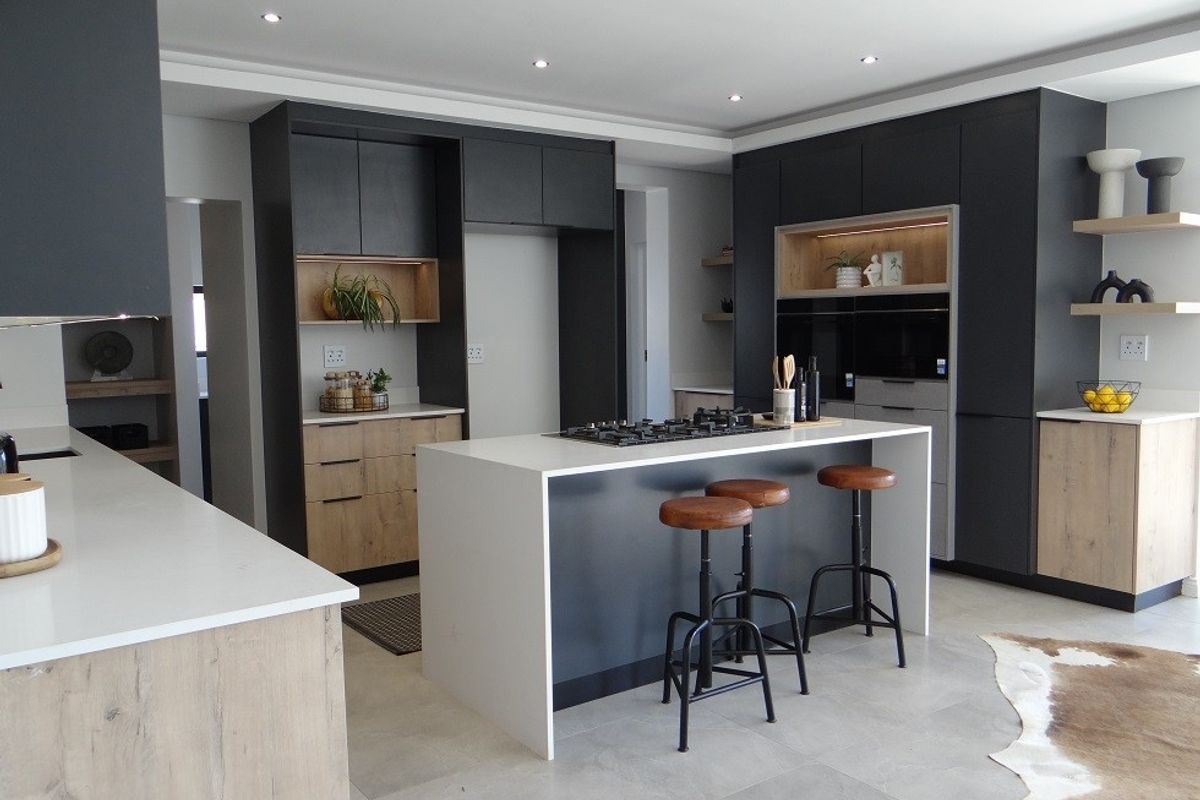 Modern kitchen featuring a central island with a gas cooktop, sleek dark cabinetry, light wood accents, and high-quality stone countertops.