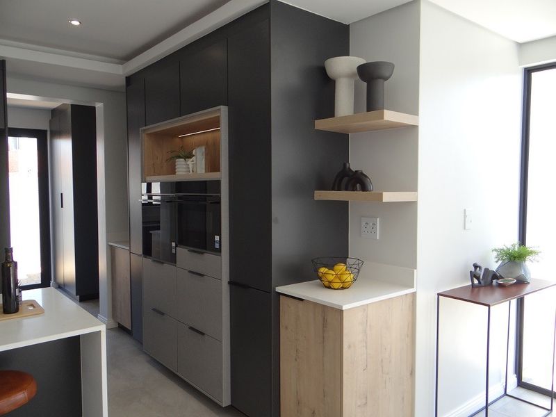 Modern kitchen featuring sleek dark cabinetry, integrated oven, stone countertops, and minimalist floating shelves with recessed lighting.
