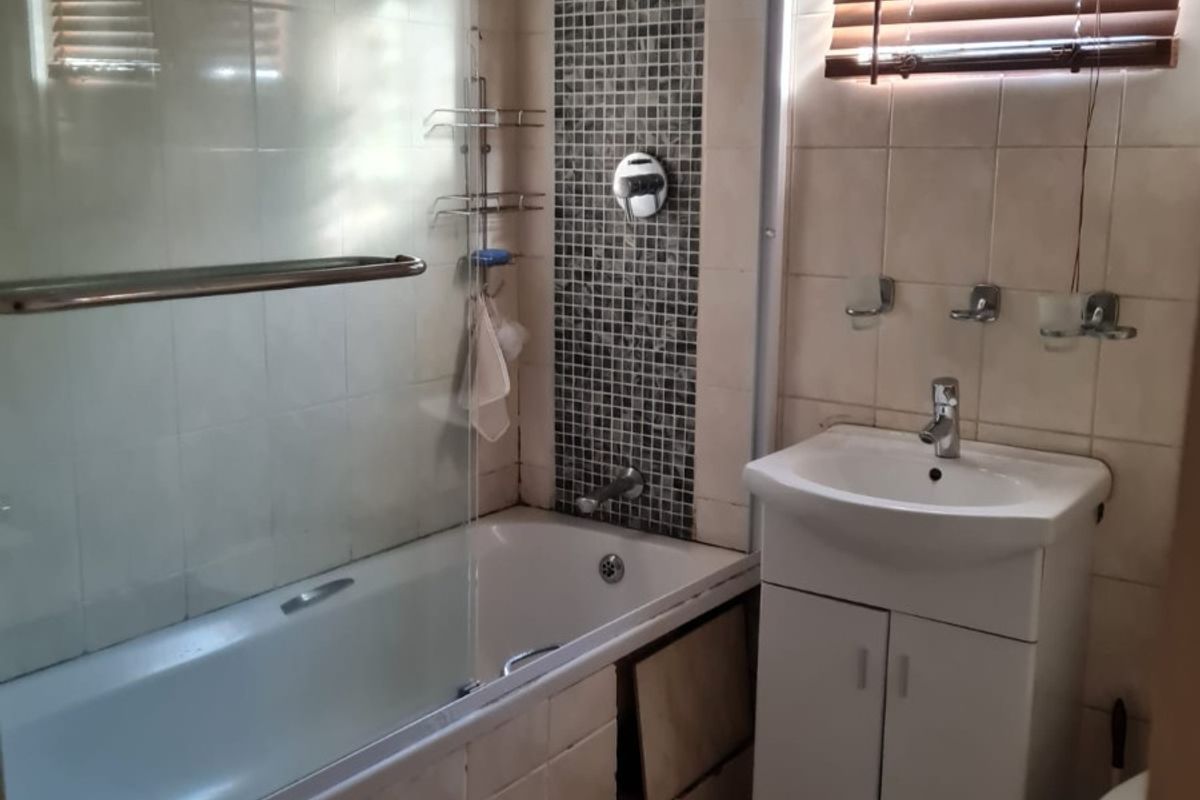 A functional bathroom featuring a bathtub with a glass shower screen, a vanity unit with a washbasin, and tiled finishes throughout.