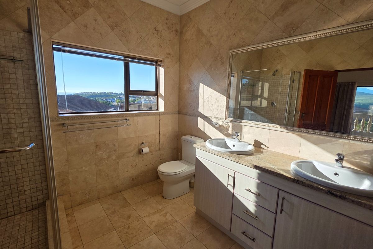 Spacious bathroom featuring a double vanity with stone countertop, dual sinks, large wall mirror, and a walk-in shower with natural stone tiling.
