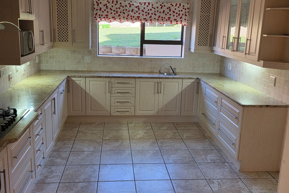 A well-maintained kitchen featuring light wood cabinetry, granite countertops, tiled flooring, and a built-in hob, offering a clean and functional workspace.