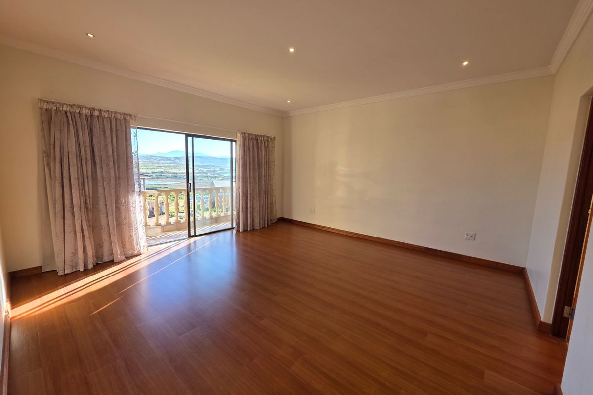 Spacious, empty bedroom featuring warm laminate flooring, recessed lighting, and a sliding glass door providing direct access to a balcony with scenic views.
