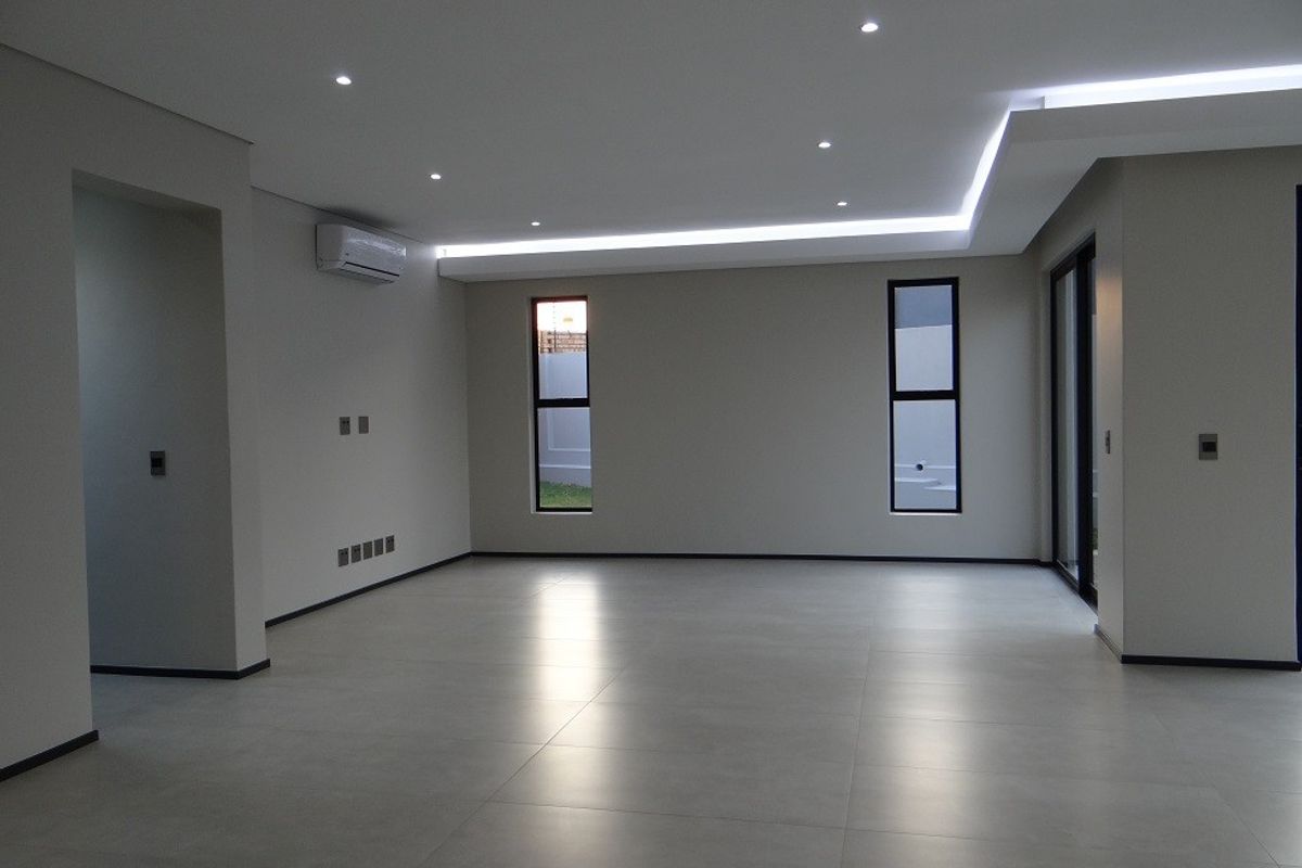 Spacious, modern living area featuring large format floor tiles, recessed and cove lighting, and a split-system air conditioner in a neutral, contemporary finish.