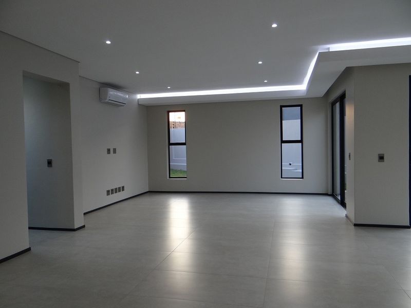 Spacious, modern living area featuring large format floor tiles, recessed and cove lighting, and a split-system air conditioner in a neutral, contemporary finish.