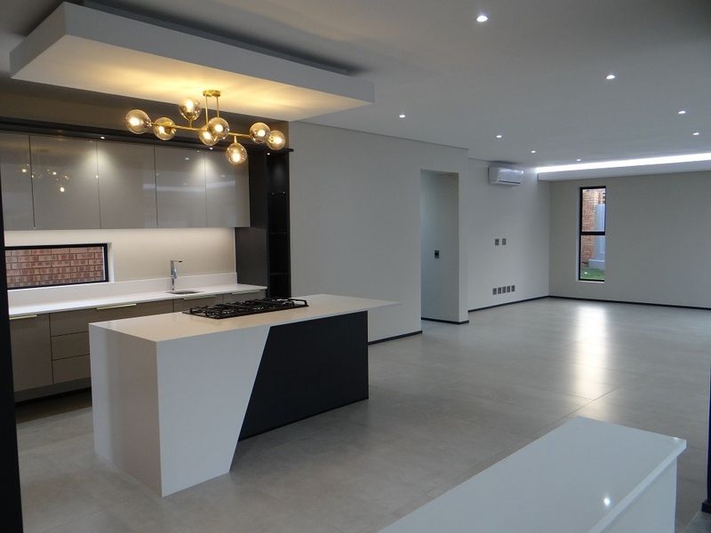 Modern open-plan living area featuring a sleek kitchen with a central island, gas cooktop, high-end cabinetry, and neutral tiled flooring throughout.