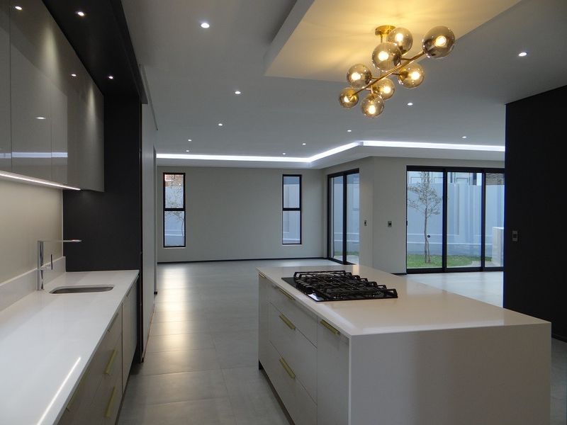 Modern open-plan kitchen and living area featuring a central island with gas hob, sleek cabinetry, recessed lighting, and large sliding doors leading to the garden.