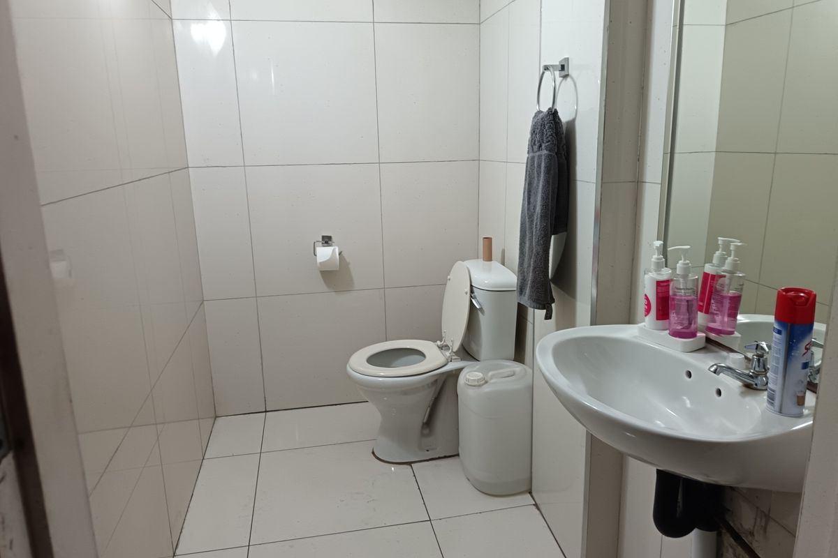 A functional bathroom featuring full-height ceramic wall tiling, a standard toilet, and a pedestal washbasin with a wall-mounted mirror.