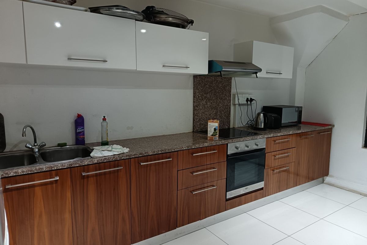 A functional kitchen featuring wood-grain lower cabinetry, white upper cabinets, granite-look countertops, and integrated appliances including an oven and hob.