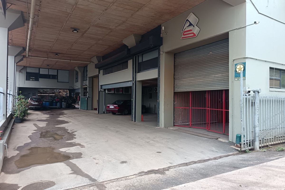 Industrial property exterior featuring a large concrete driveway, covered loading area with roller shutter door, and secure perimeter fencing.