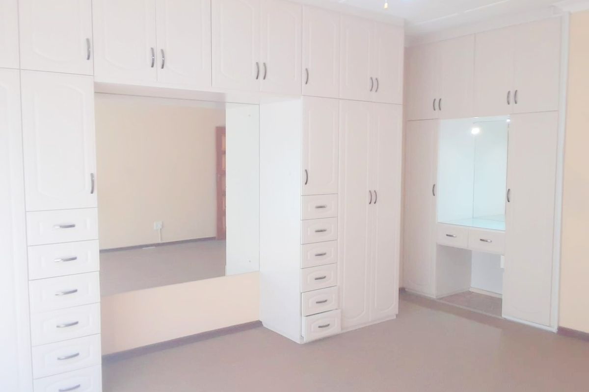 Spacious bedroom featuring extensive built-in cabinetry with integrated vanity and mirrored sections, offering ample storage and a functional layout.