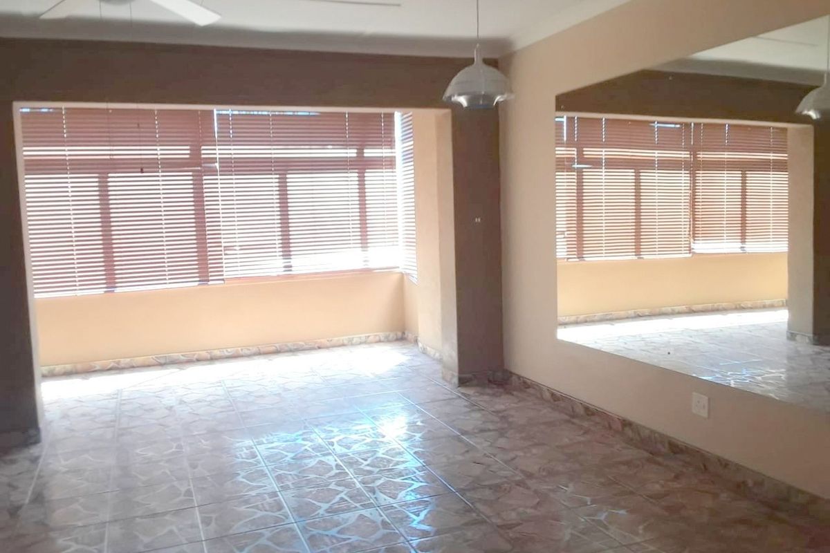 Spacious living area featuring tiled flooring, a large wall mirror, ceiling fan, and natural light through venetian blinds.