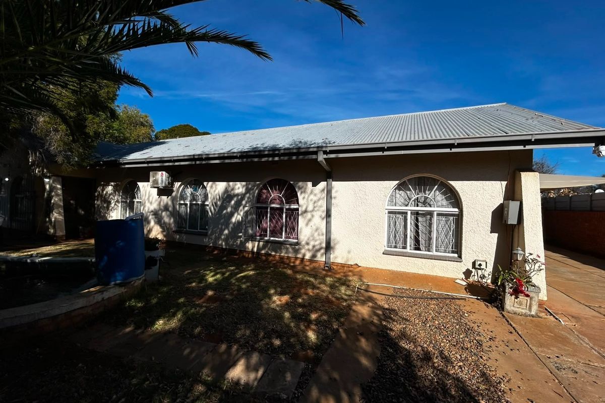 Rear exterior view of the house featuring a corrugated metal roof, arched windows with security bars, and a paved pathway.