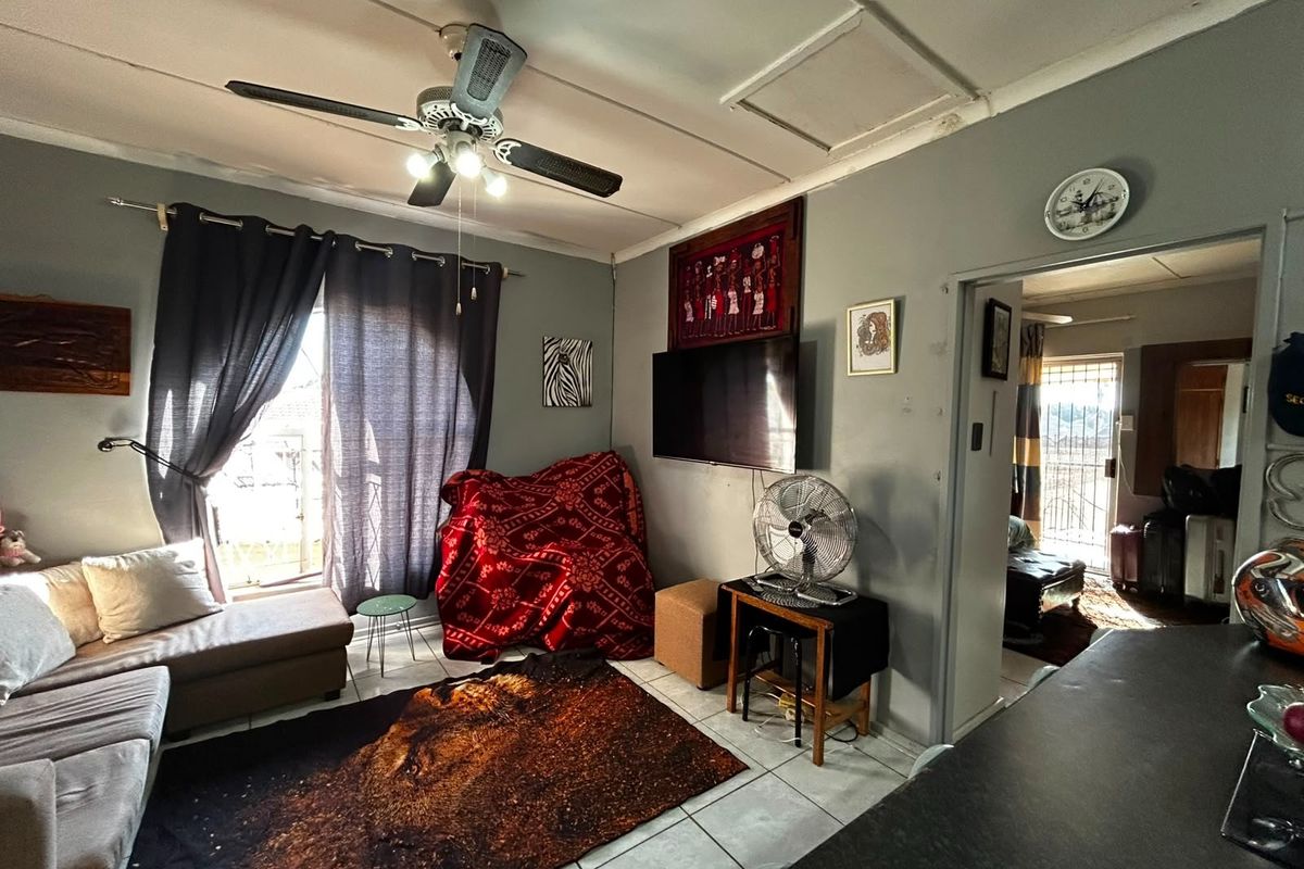 Living room featuring tiled flooring and a ceiling fan, with access to an adjacent room and exterior area.