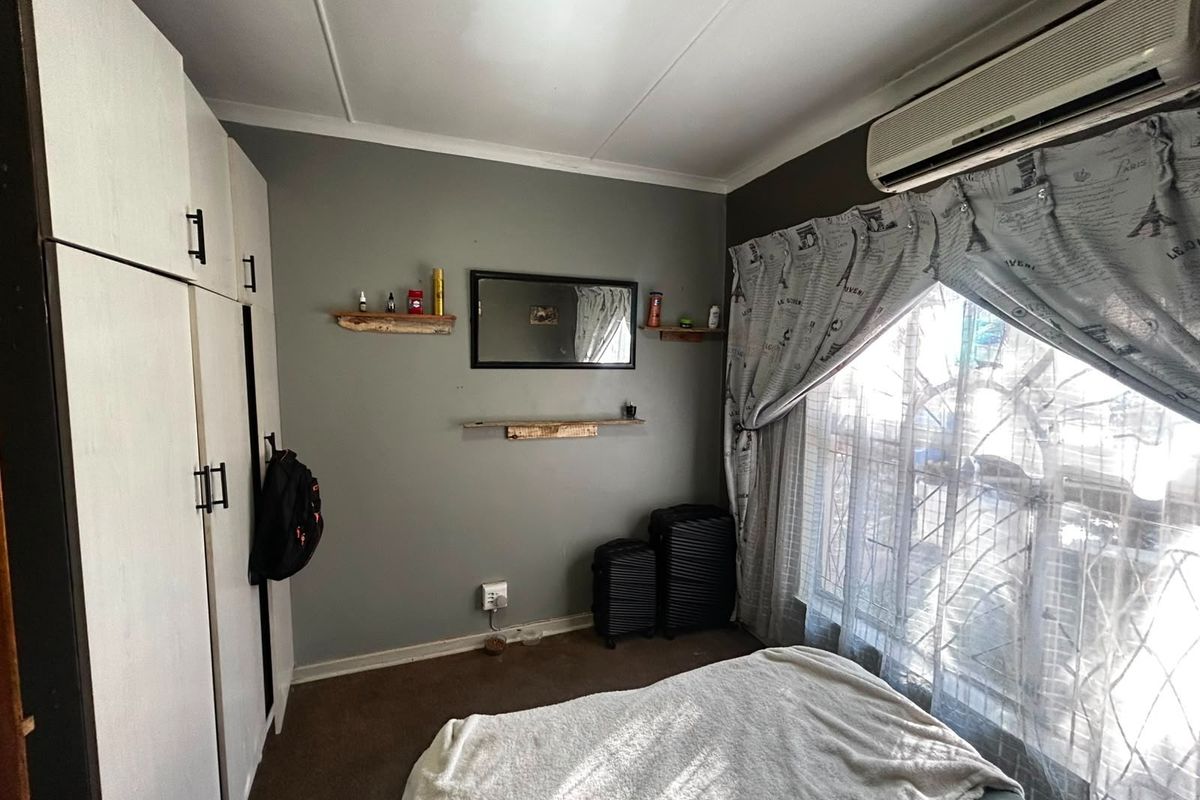 A functional bedroom featuring built-in cupboards, a wall-mounted air conditioning unit, and security bars on the window.