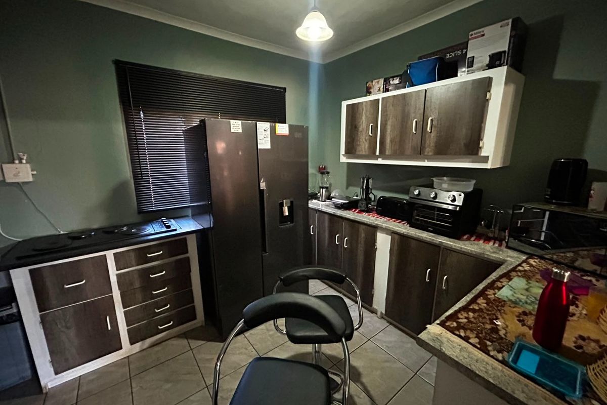 A functional kitchen featuring dark wood-look cabinetry, laminate countertops, and ceramic floor tiles, providing a practical workspace with integrated hob and storage.