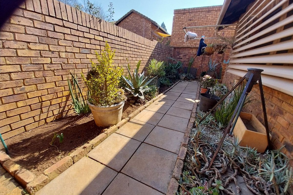 A narrow rear garden area featuring a paved walkway, brick boundary walls, and established garden beds.