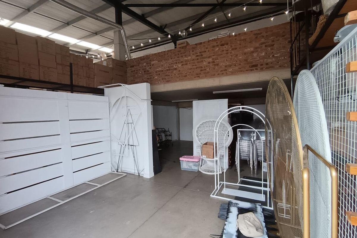 Spacious commercial utility area featuring exposed brick mezzanine level, high steel roof trusses, and durable concrete flooring, suitable for storage or workshop use.