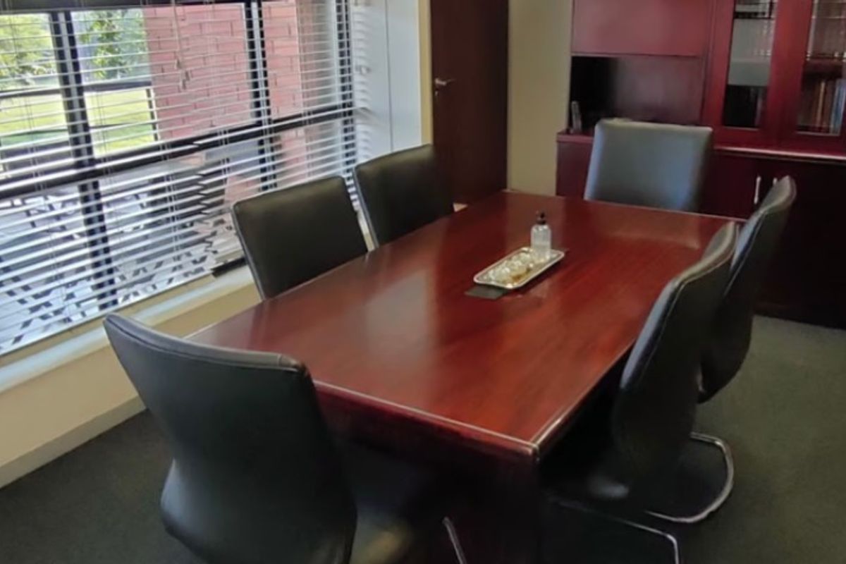 A professional office meeting room featuring built-in dark wood cabinetry and large windows with venetian blinds.