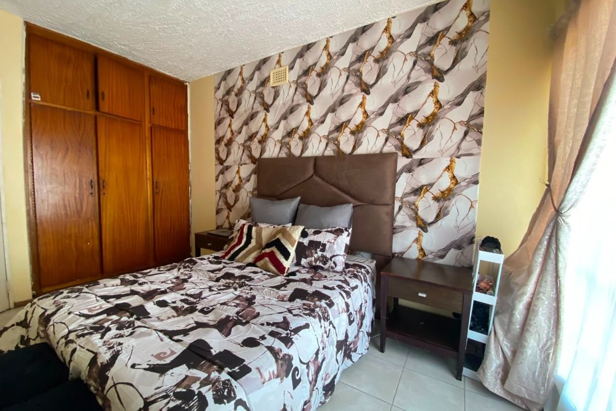 A bedroom featuring built-in wooden cupboards, tiled flooring, and a decorative feature wall.