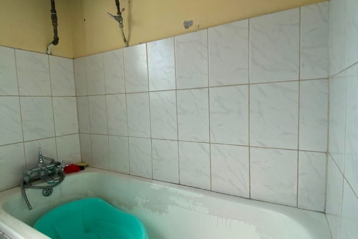 A bathroom featuring a bathtub with wall-mounted electric water heater and tiled walls, showing signs of wear and requiring cosmetic updates.