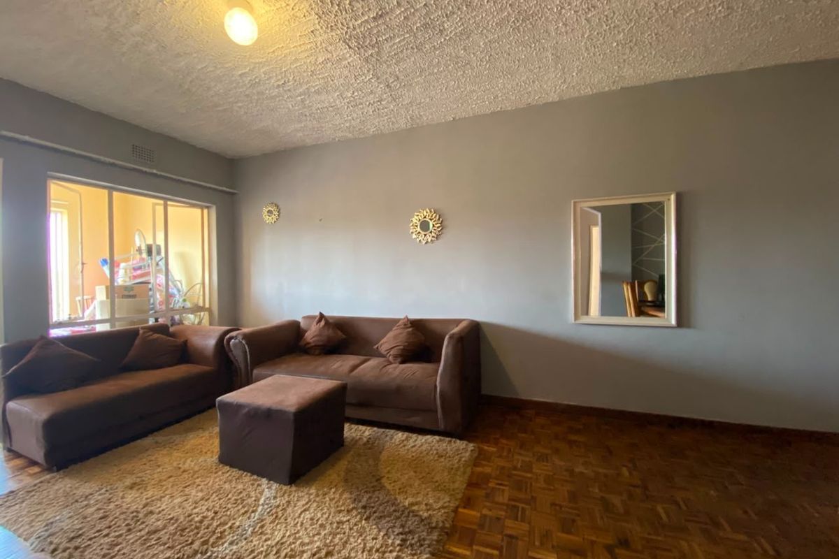 A living room featuring classic parquet flooring, a textured ceiling, and a large window providing natural light.