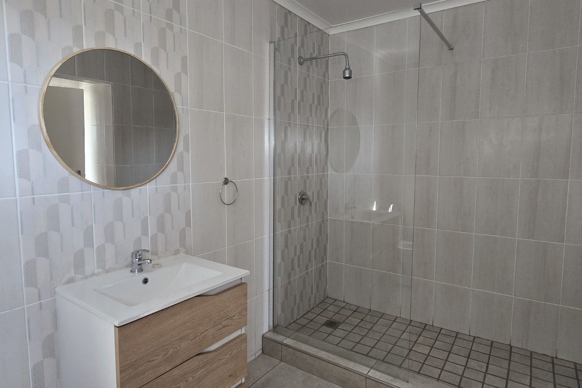 Modern bathroom featuring a spacious walk-in shower with glass screen, contemporary vanity cabinet with basin, and neutral wall tiling.