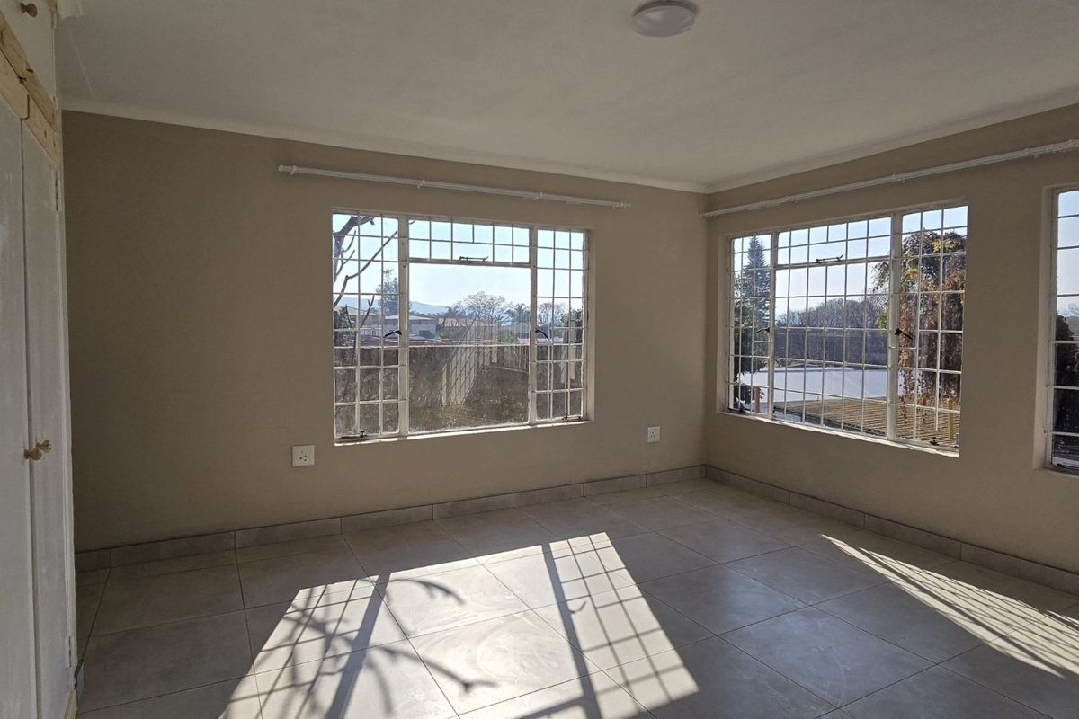 A bright, empty bedroom featuring tiled flooring, built-in cupboards, and large steel-framed windows with security bars, offering ample natural light.