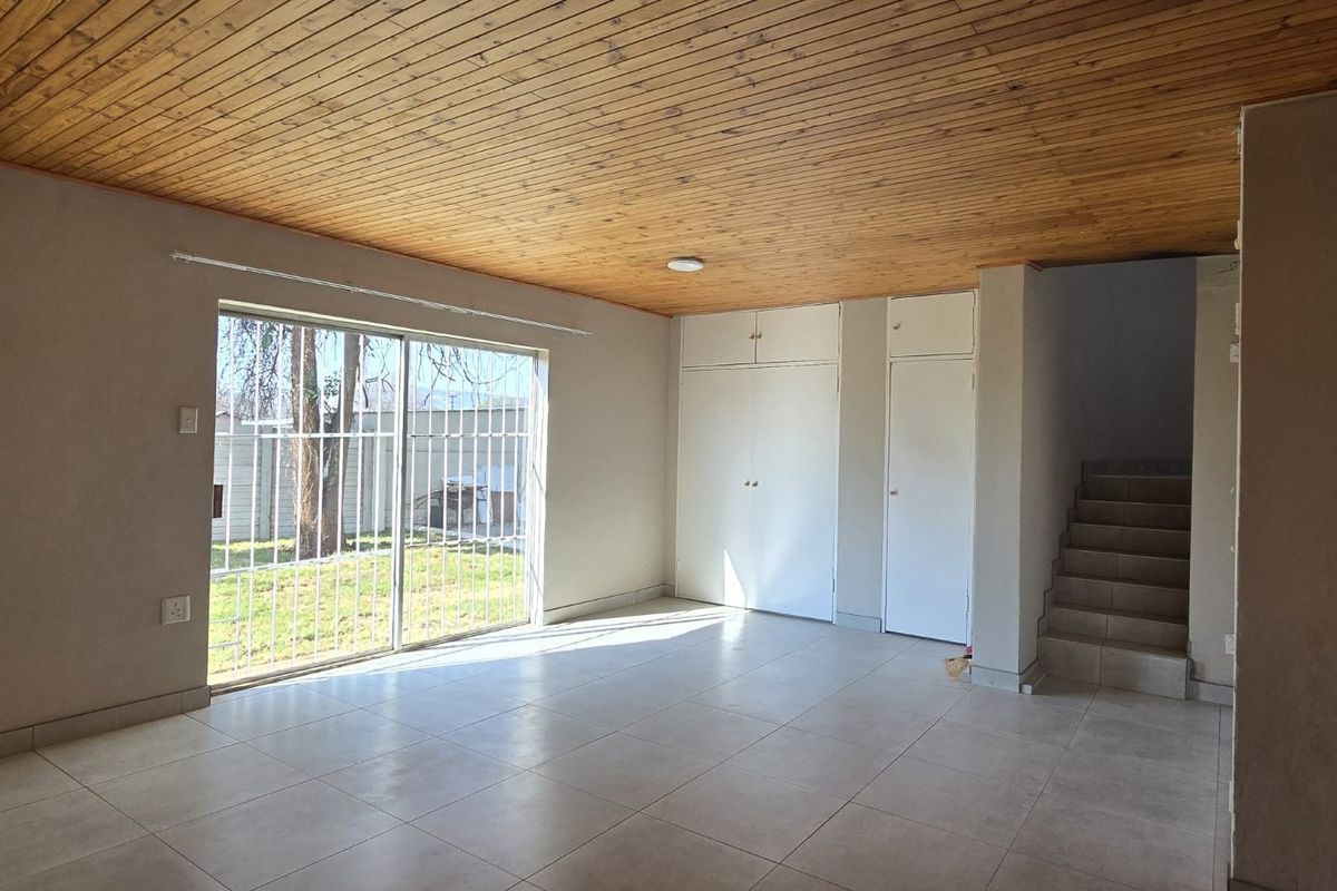 Spacious living area featuring a timber ceiling, tiled flooring, built-in storage cupboards, and a sliding glass door providing direct access to the garden.