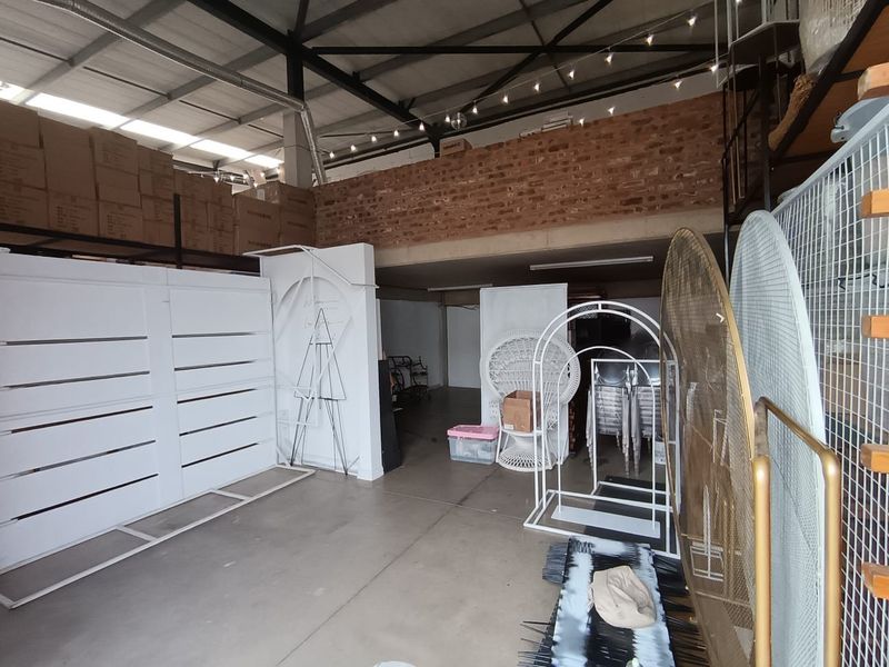Spacious commercial utility area featuring exposed brick mezzanine level, high steel roof trusses, and durable concrete flooring, suitable for storage or workshop use.