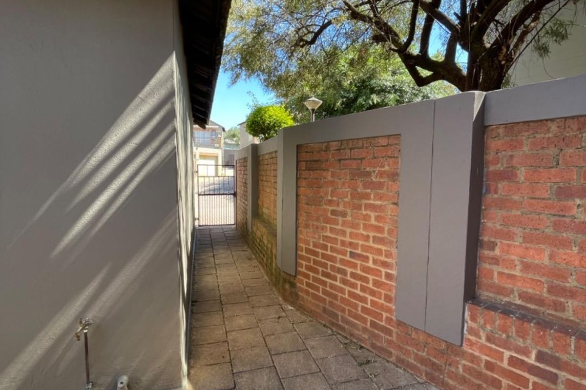 A side walkway featuring paved flooring, a brick boundary wall, and an external water tap, leading towards a metal security gate.