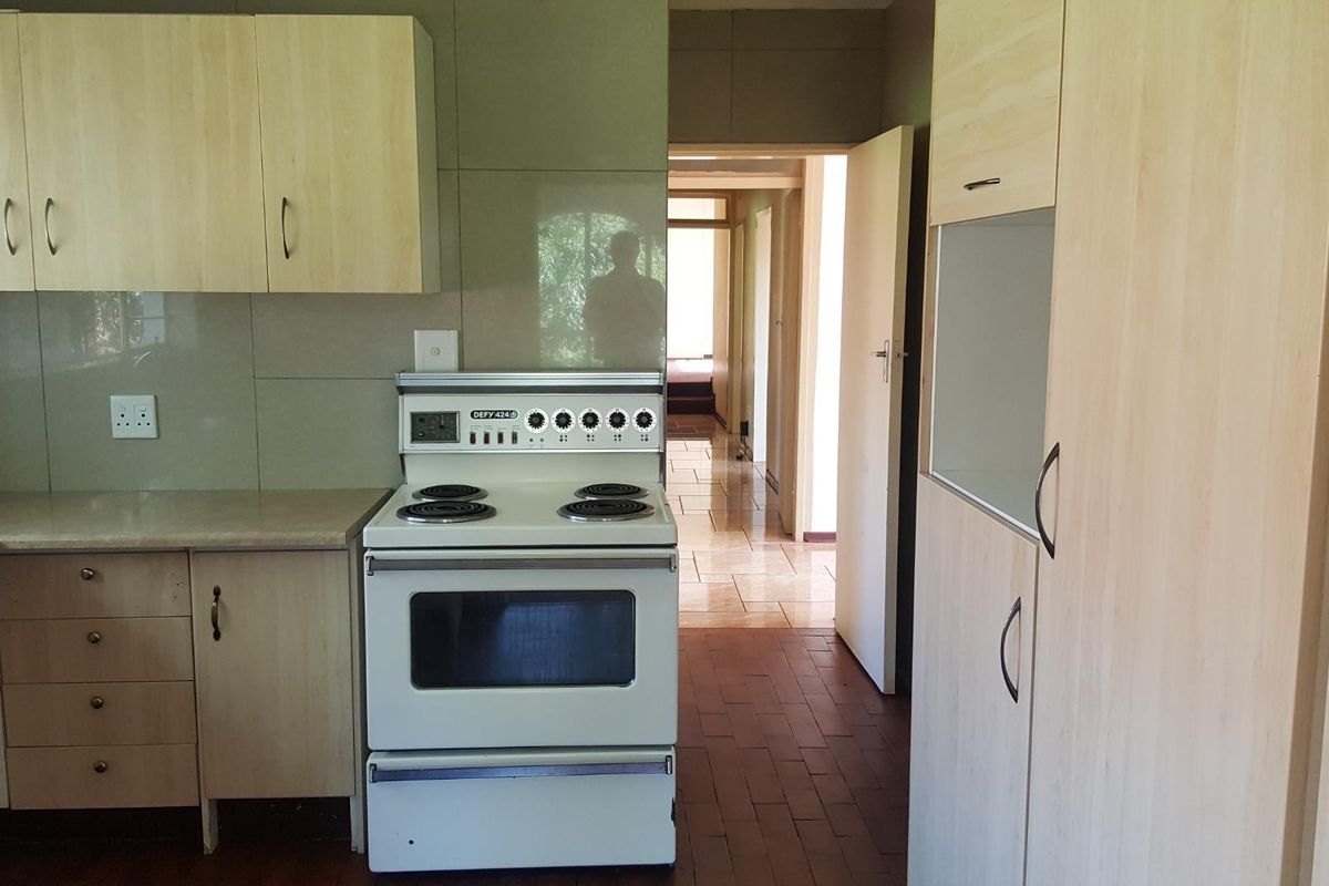 A functional kitchen featuring light wood-look cabinetry, tiled splashbacks, and a freestanding electric stove, leading into a tiled hallway.