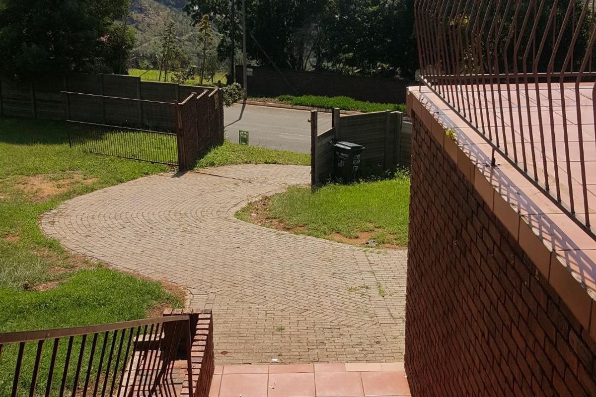 Outdoor view from a tiled patio down a brick staircase to a paved driveway and garden area with distant landscape views.