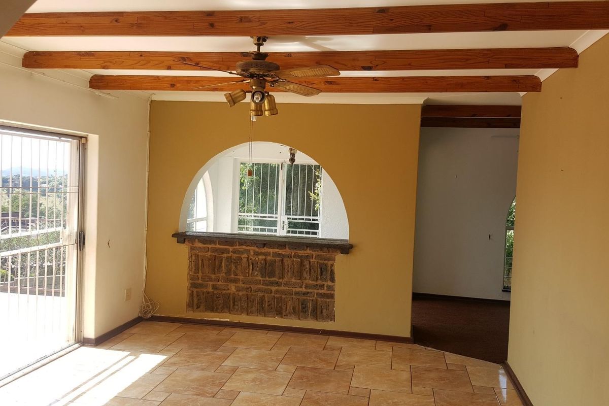 Spacious living area featuring exposed timber ceiling beams, tiled flooring, and a unique brick archway, offering a bright and open layout.