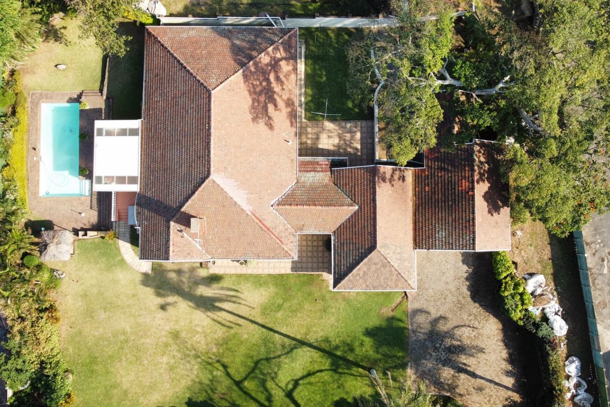 Aerial view of the property showcasing the tiled roof, swimming pool, paved patio areas, and surrounding garden space.