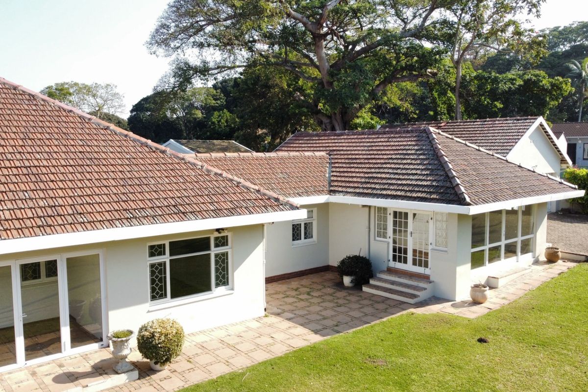 Aerial view of the rear exterior featuring a tiled roof, paved patio area, and access through multiple sets of french doors to the garden.