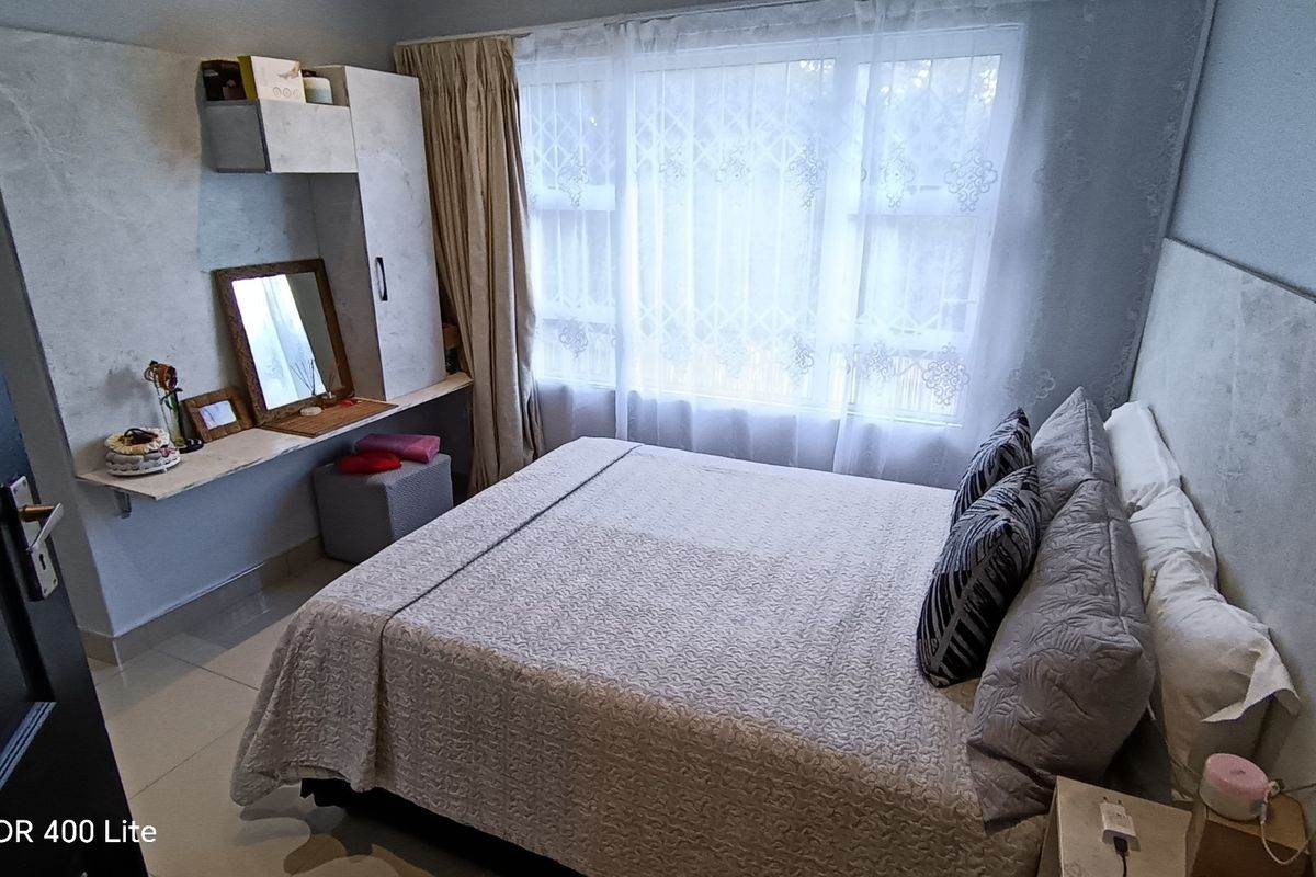 A well-maintained bedroom featuring tiled flooring, a built-in vanity unit, and a large window fitted with a security gate.