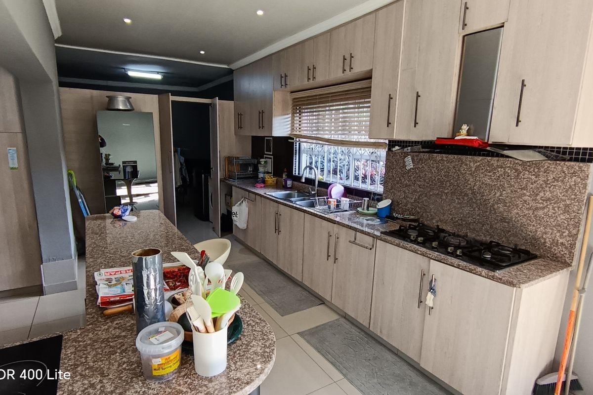 A functional kitchen featuring light wood cabinetry, granite countertops, a gas hob, and tiled flooring with ample storage space.