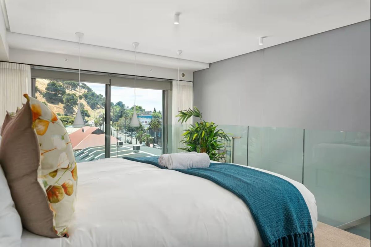 Modern bedroom featuring a glass balustrade, recessed lighting, and large sliding doors offering expansive views of the surrounding area.