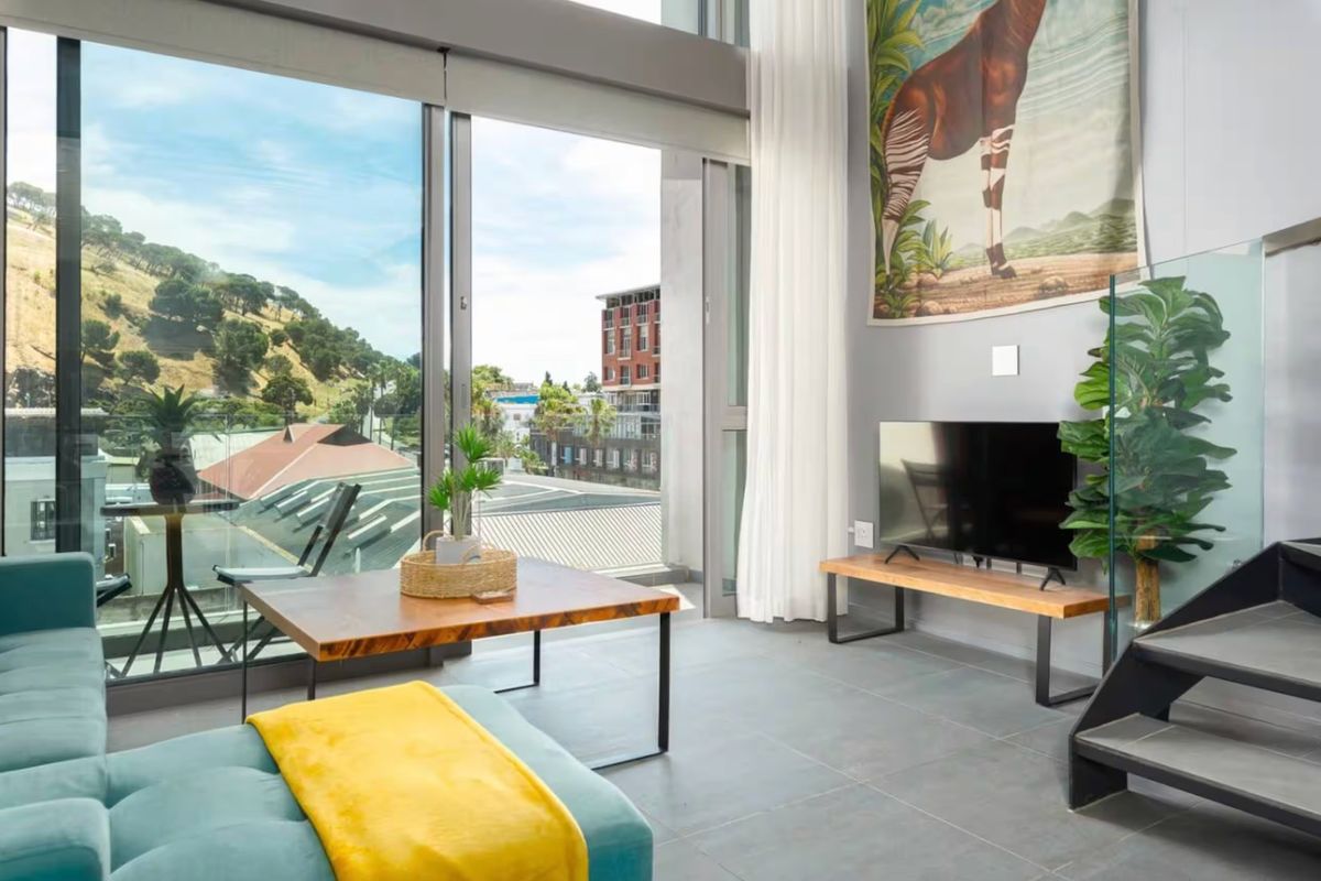 Modern living room featuring floor-to-ceiling windows, tiled flooring, and a staircase, offering bright natural light and access to a balcony with urban views.