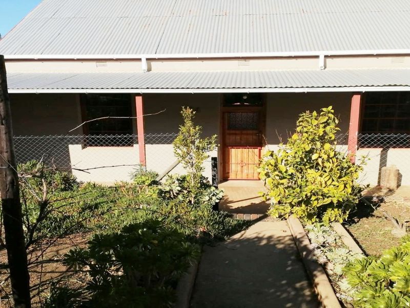 Front elevation of a house featuring a corrugated metal roof, covered veranda, and a concrete pathway leading to the main entrance.