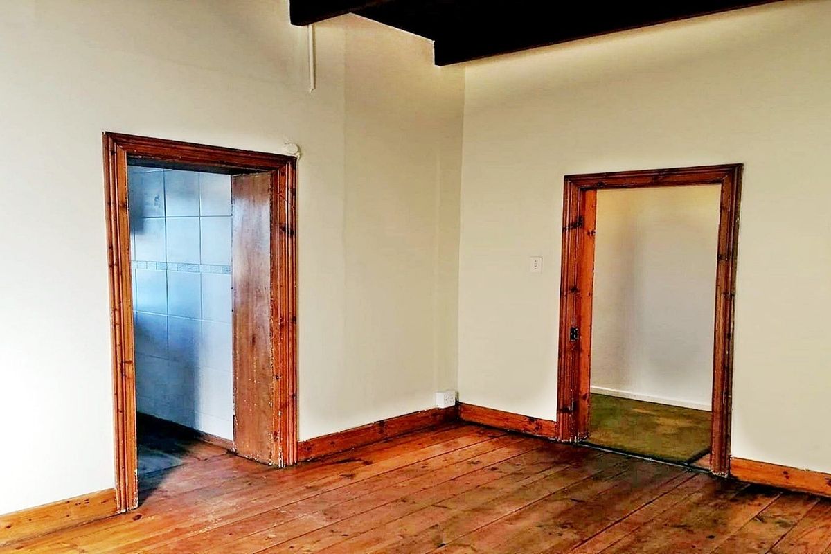 An empty living area featuring original timber floorboards, exposed ceiling beams, and classic timber door frames leading to adjacent rooms.