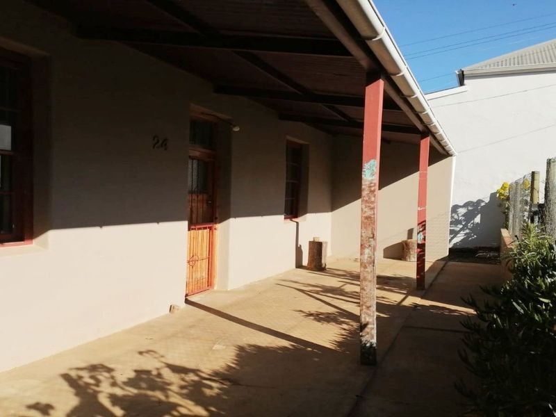 A covered outdoor patio area featuring timber support posts and a security gate entrance, showing signs of wear and requiring maintenance.