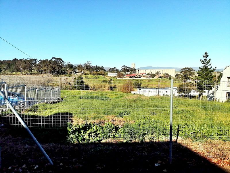 An elevated view overlooking an open grassy field and surrounding landscape, framed by wire mesh perimeter fencing.