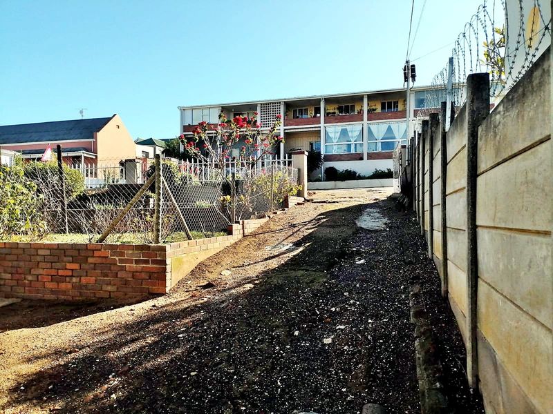 Exterior view of the property frontage featuring a gravel driveway, precast concrete boundary wall with razor wire, and a brick retaining wall.
